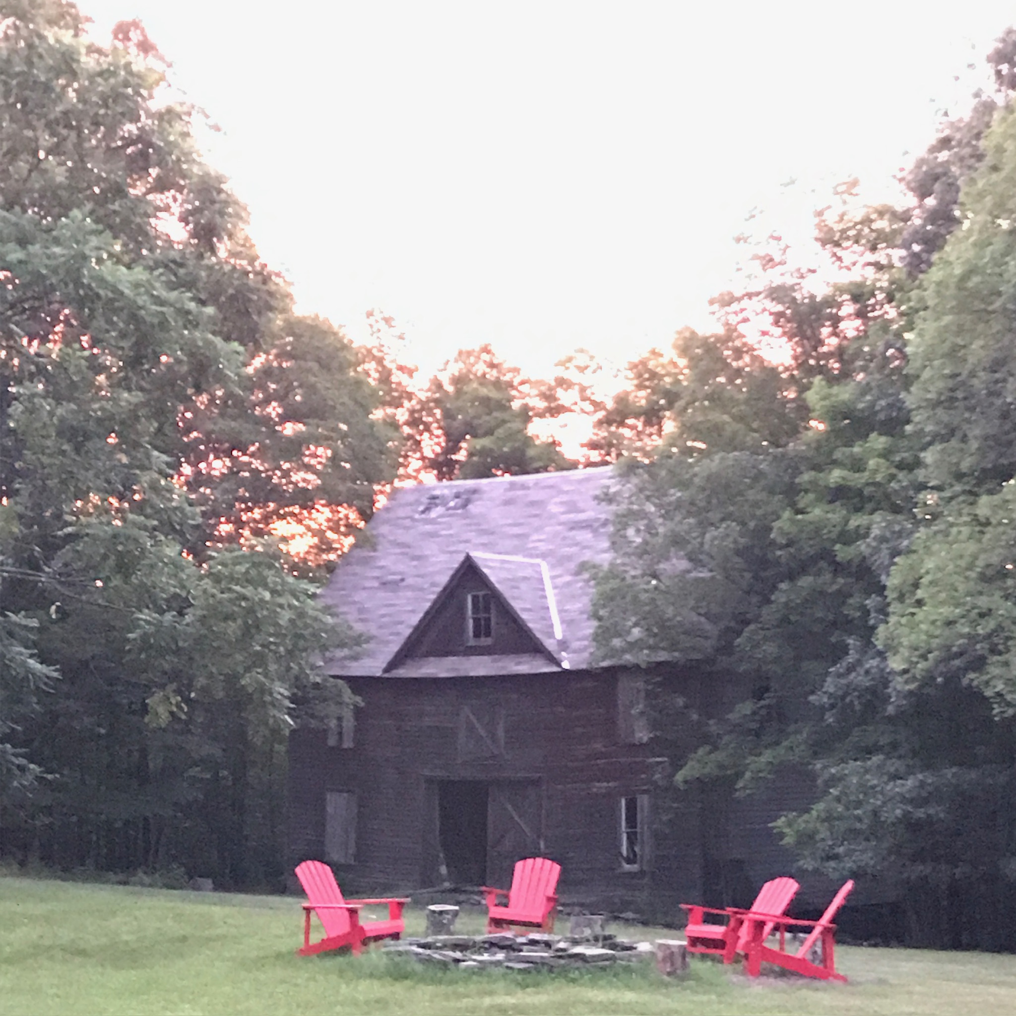 The barn at dusk with red Adirondack chairs and fire circle in the foreground