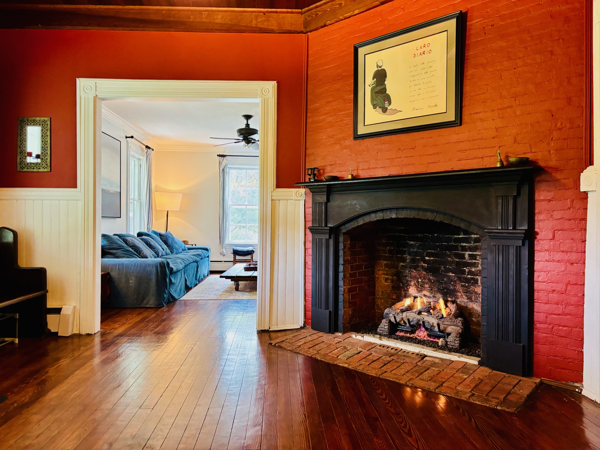 Entry hall with original fireplace, red painted brick surround, black mantle, and fire burning in the hearth