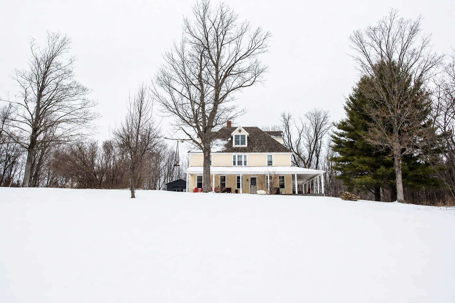 Elliot Place farmhouse in winter, the full yellow exterior and wrap-around porch visible across a snow-covered lawn