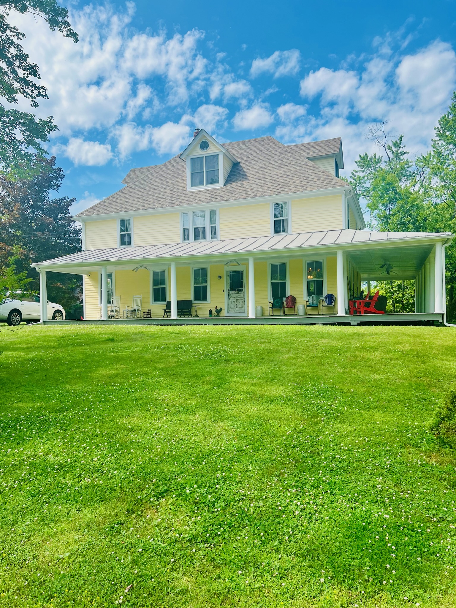 Ground-level view of the farmhouse and wrap-around porch on a sunny day