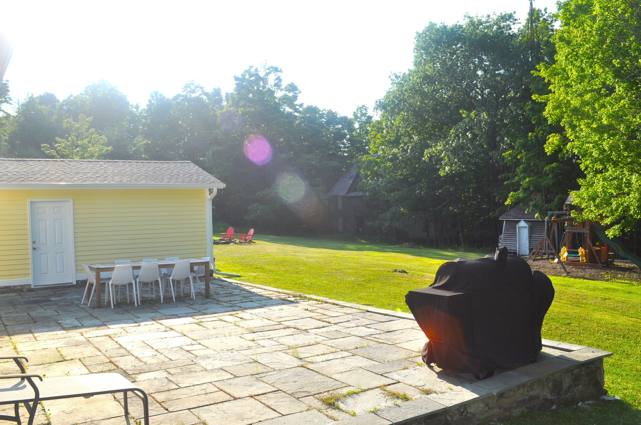 The bluestone patio with dining table, overlooking the lawn and play set