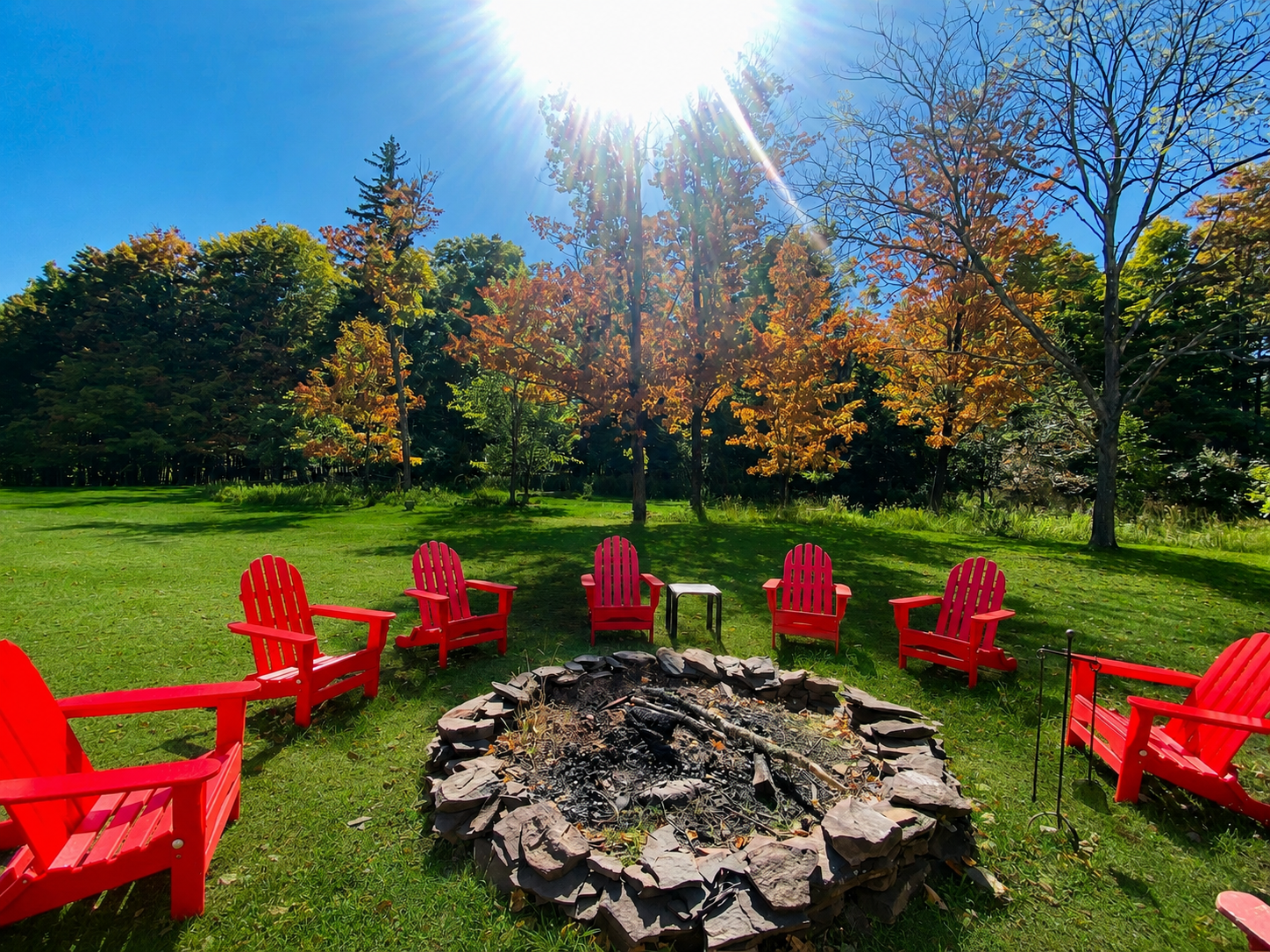 The fire pit circle ringed by red Adirondack chairs, framed by peak fall foliage