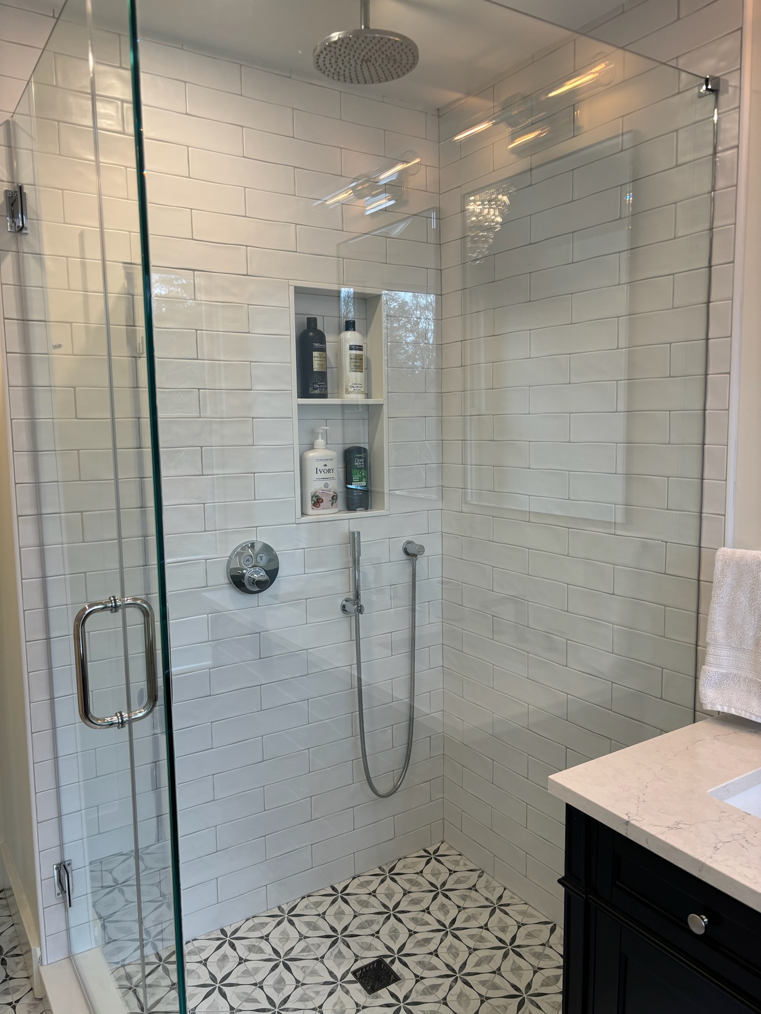 Master bathroom glass-enclosed rain shower with white subway tile and geometric mosaic floor tile