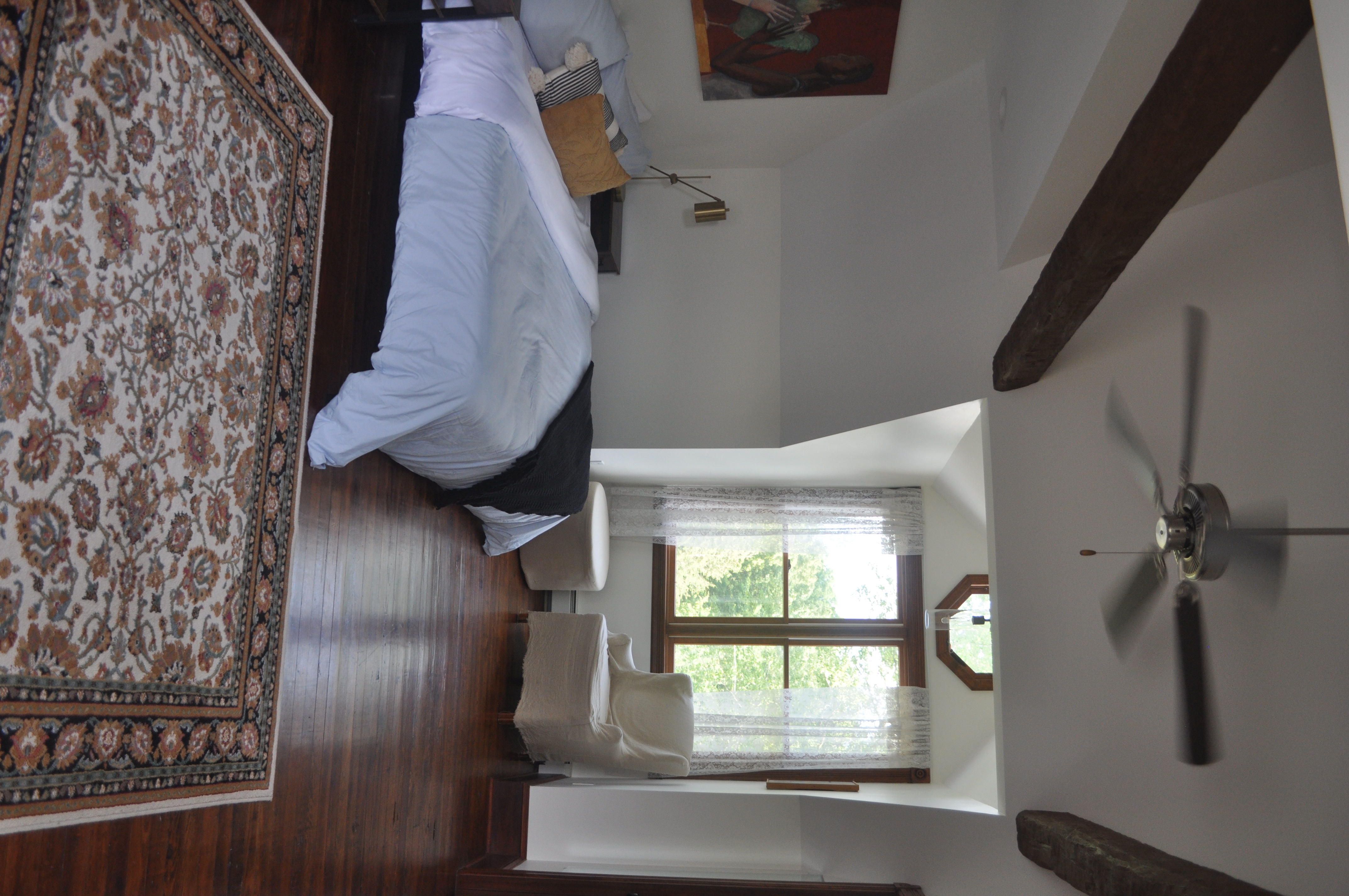 The master bedroom with cathedral ceiling, exposed timber beams, king bed, wood stove with vintage typewriter, and French doors to private balcony