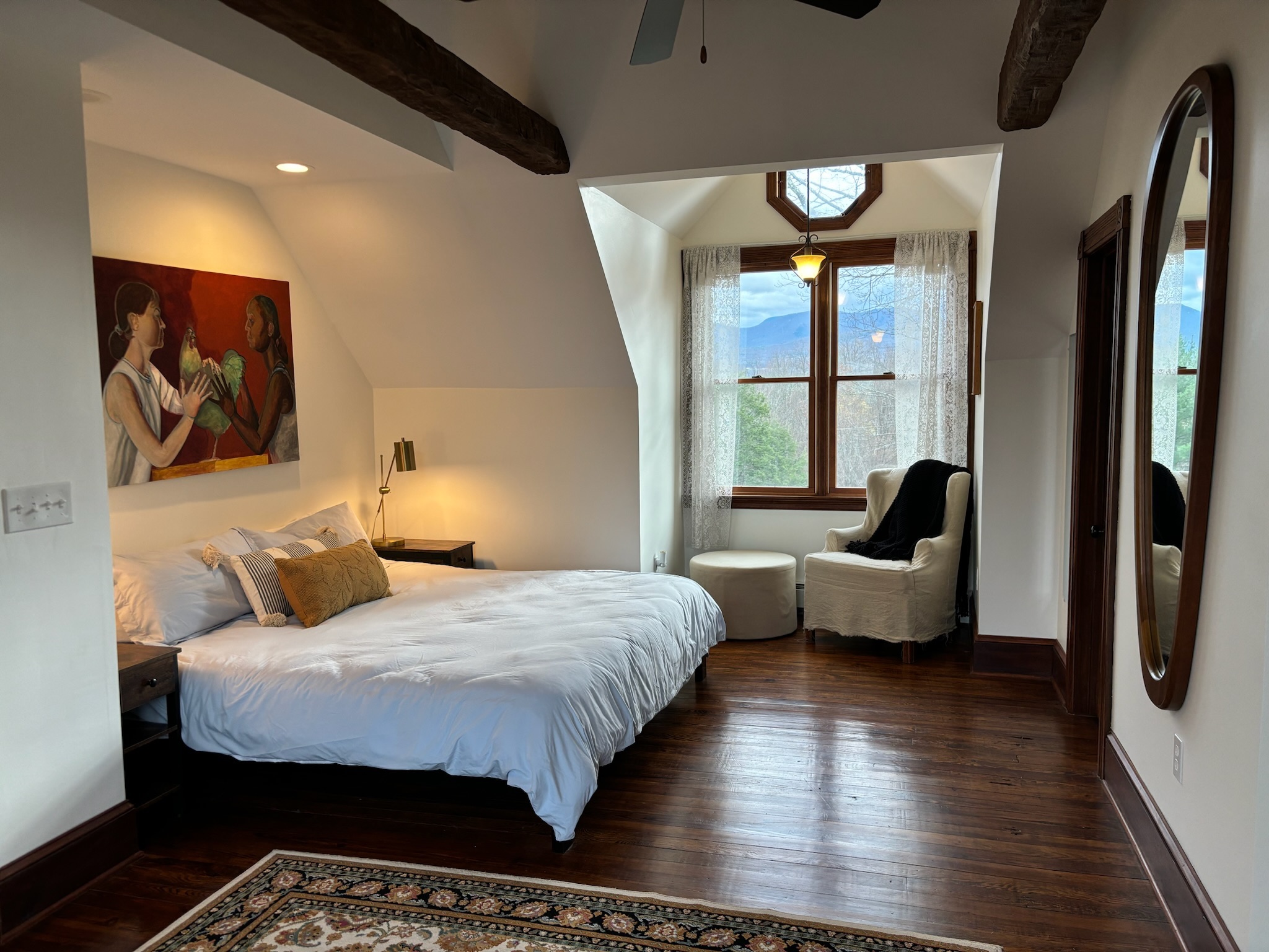 Master bedroom with king bed, reading nook wingback chair, and Catskill mountain views through lace-curtained window