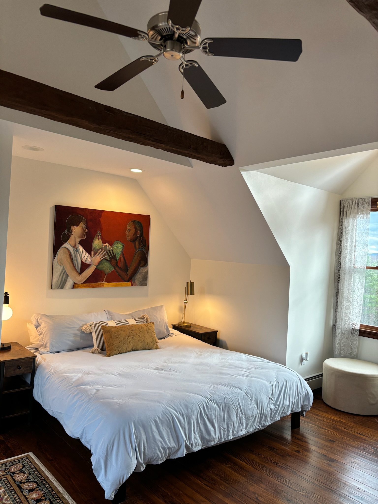 Master bedroom from foot of king bed, figurative painting above headboard, exposed timber beams and ceiling fan