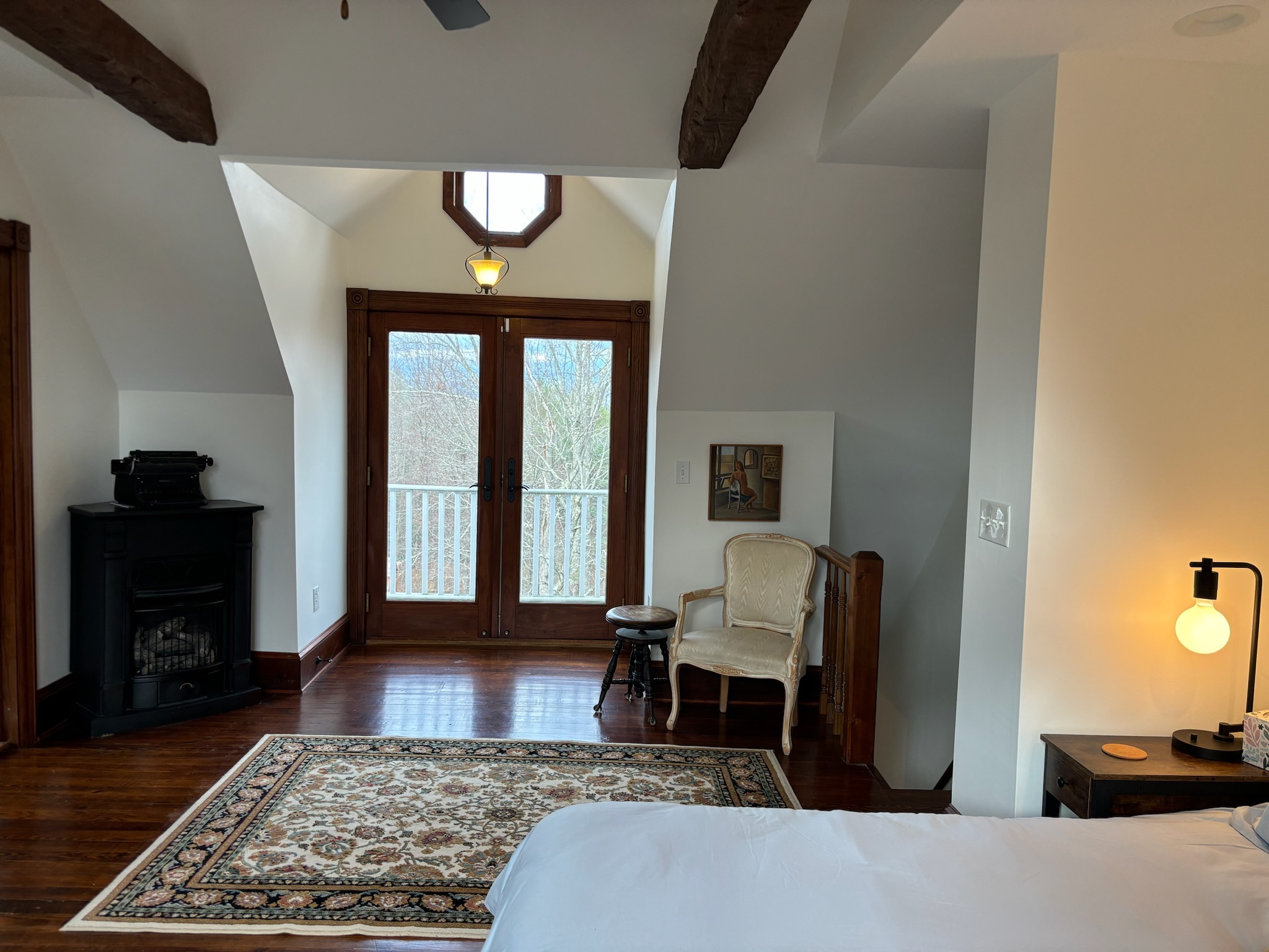 Master bedroom showing balcony French doors, wood stove with vintage Remington typewriter, Persian rug and nightstand