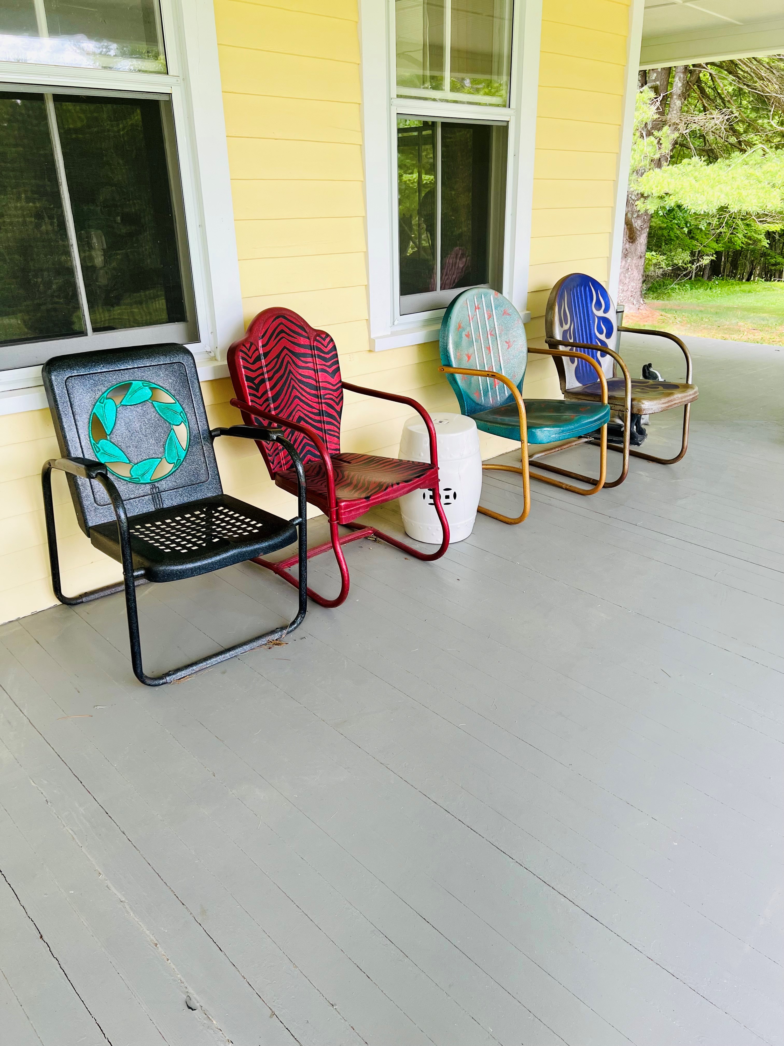 A colorful row of vintage metal porch chairs against the yellow farmhouse siding