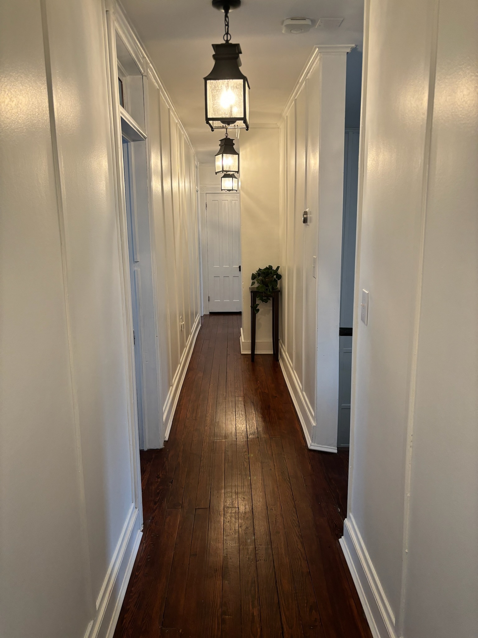 Second floor hallway with three hanging black lantern pendants, white paneled walls, and wide-plank hardwood floors